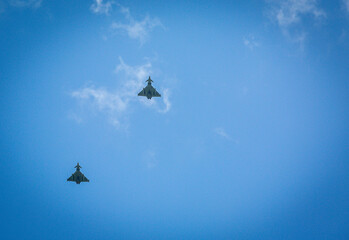 Two RAF typhoons flying, flying in formation back to their respected air fields after taking part in the kings fly past on a beautiful summers day with blue skies and slight cloud