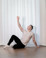 A man in a classical ballet dance pose. Dance training for home. A young and handsome dancing guy in sports poses.