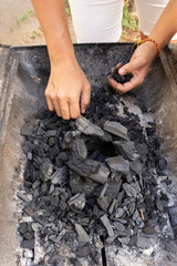 Vertical photography of hands over the charcoal in the grill.