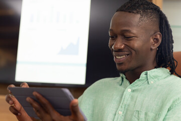 Using tablet, man smiling while analyzing financial data on screen in office