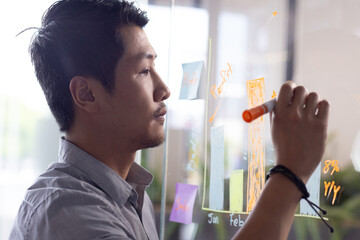 Writing on transparent board, man analyzing data and creating business strategy