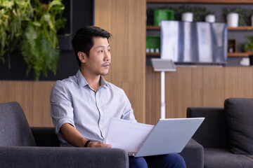 Holding documents and using laptop, man working in modern office setting