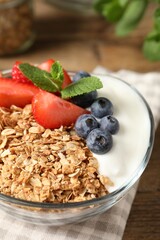 Tasty granola with berries and yogurt in bowl on wooden table, closeup
