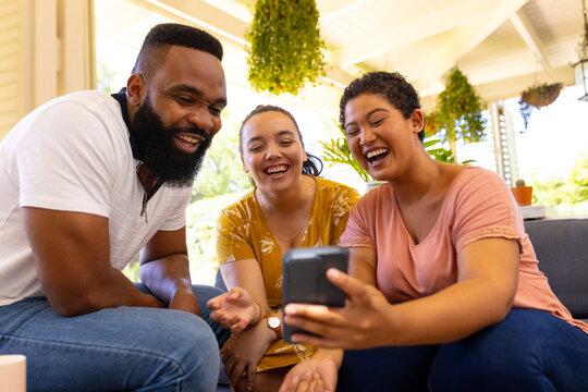 undefined sitting together, smiling and looking at smartphone, enjoying time at home