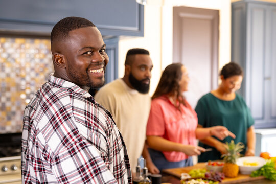 Smiling man in kitchen with diverse friends preparing food and enjoying time together