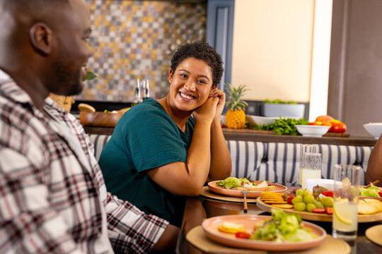 Smiling woman enjoying meal with diverse friends, sitting at dining table with food