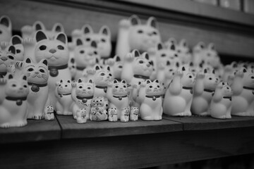 A black and white photo of shelves overflowing with Maneki-neko cat figurines of various sizes in Gotokuji Temple