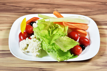 Warm salad with  lettuce, cherry tomatoes, slices of yellow bell pepper, olives, sticks of celery and carrot sticks. 