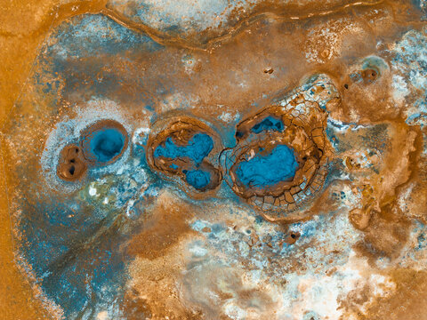 Aerial view of Hverir Geothermal Area, Iceland, showcasing vibrant blue and orange geothermal pools and mud pits in a surreal landscape.