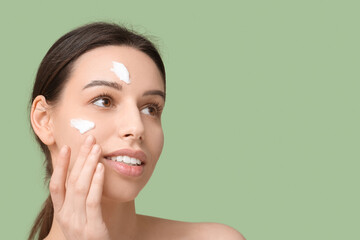 Beautiful young woman with cream on face against green background