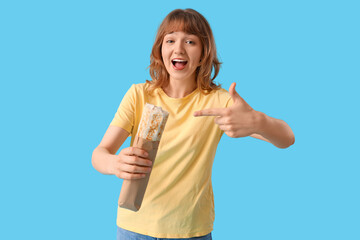 Fototapeta premium Young woman pointing at doner kebab on blue background