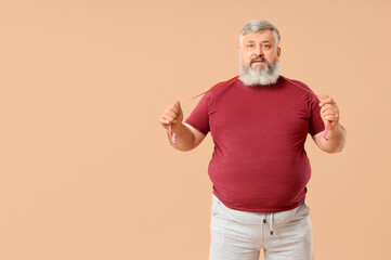 Overweight mature man with jumping rope on beige background. Weight loss concept