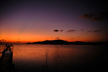 Golden hues of sunset paint the sky and reflect on the tranquil waters, creating a serene and picturesque scene by the pier