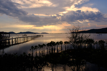 Golden hues of sunset paint the sky and reflect on the tranquil waters, creating a serene and picturesque scene by the pier