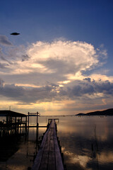 Golden hues of sunset paint the sky and reflect on the tranquil waters, creating a serene and picturesque scene by the pier