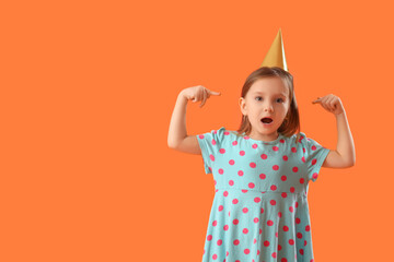Shocked little girl pointing at party cone on orange background
