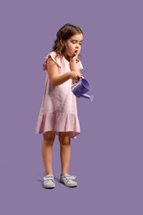 Shocked little girl with watering can on purple background