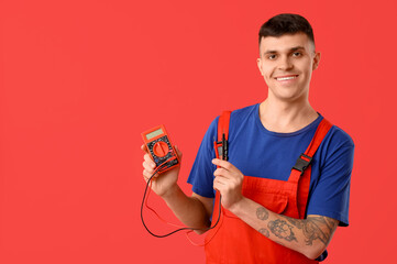 Young male electrician with multimeter on red background