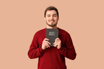 Religious young man with Holy Bible on brown background