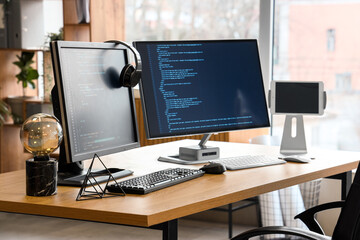 Computer monitors with programming code and headphones on desk in office