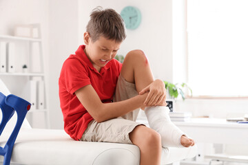 Little boy with wounded knee sitting on couch in clinic