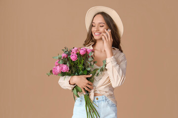 Beautiful young woman with roses talking by mobile phone on brown background