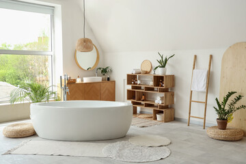 Interior of light bathroom with ceramic bathtub and houseplants