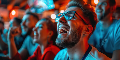Obraz premium Bearded man with glasses, laughing and enjoying a sports event with friends in a lively, vibrant atmosphere.