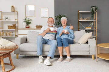Obraz premium Mature woman after chemotherapy with her husband drinking tea on sofa at home