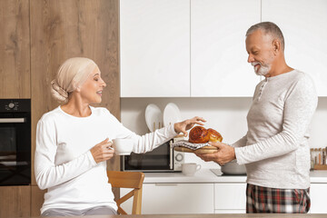 Mature woman after chemotherapy taking bun from her husband in kitchen