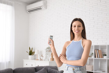 Pretty young woman with air conditioner remote control at home