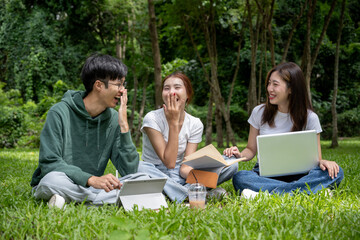 A group of cheerful Asian students in casual clothes sits and talks in the green park, enjoying their conversation while working on their co-project together.