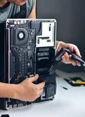 A technician is removing an old, damaged battery from a laptop.