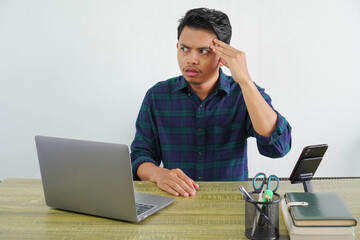 Bewildered young asian man sit work at wooden desk with pc laptop. Achievement business career lifestyle concept. Put hand on head