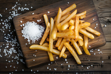 Top view of French fries on wooden board with some salt on side. Generative AI