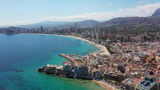 Aerial drone footage of the beautiful city of Benidorm in Spain in the summer time showing the Playa de Levante beach and the area known as old town with the boating harbour and look out point