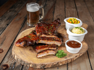 Baby back ribs with buttered vegetables, mashed potatoes, barbecue sauce and beer on wooden board and table