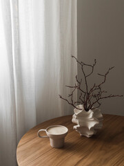 Cappuccino cup, creative ceramic vase with dry branches on a round wooden table