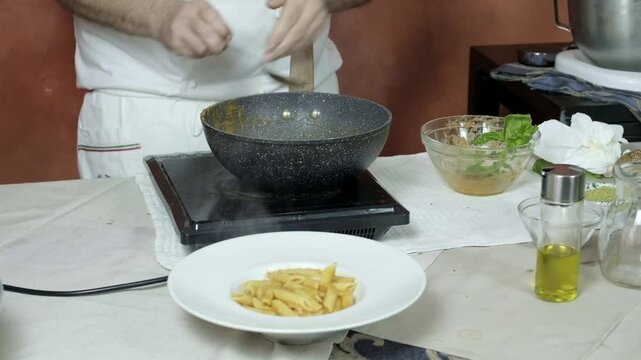 Chef plates penne pasta onto deep dish and adds roasted veggies to create pasta norma dish ready for presentation