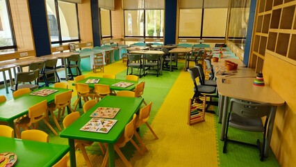 class room of kidergarten. Yellow and green theme based study room for toddlers to learn, play and get educated. tables and chairs are placed inside along with games for kids to play. 