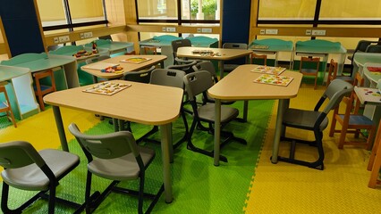 class room of kidergarten. Yellow and green theme based study room for toddlers to learn, play and get educated. tables and chairs are placed inside along with games for kids to play. 