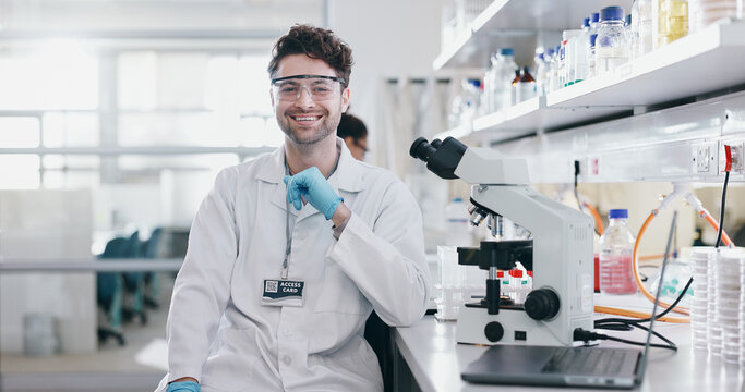 Portrait, science and smile of man on microscope in lab to research chemistry, test or innovation. Laptop, scientist and face of medical doctor in goggles for microbiology, healthcare or pharma study