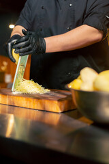 close up in a restaurant in rib bar in the central hall a chef in black gloves grates potatoes on a...