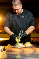 close up in a restaurant in rib bar in the central hall a chef in black gloves grates potatoes on a...