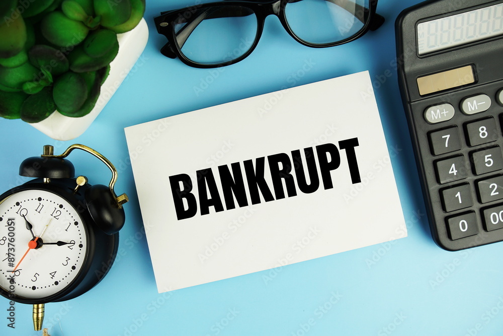 Poster bankrupt text on paper card with alarm clock and calculator top view on blue background