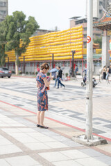 Young Taiwanese woman in her 20s wearing blue cheongsam strolling and drinking bubble tea in front of Longshan Temple, Wanhua District, Taipei, Taiwan