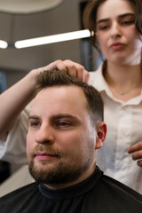 Haircut of a visitor in a barbershop. Hair styling with a hand, combing the client's hair by a stylist.