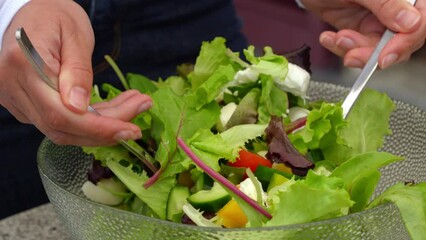 Women's hands mix salad with tomato tomato mozzarella vegetables and arugula in a large bowl for an easy diet lunch or dinner, a healthy balanced meal