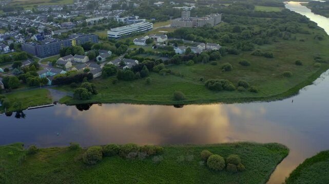 Glowing soft orange light across clouds in sky reflects on river corrib in Galway Ireland