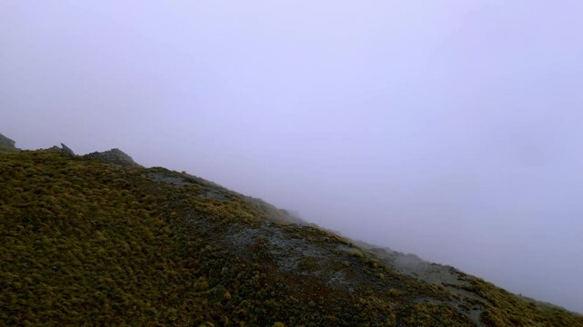 Aerial view flying over a mountain ridge disappearing into white out conditions.